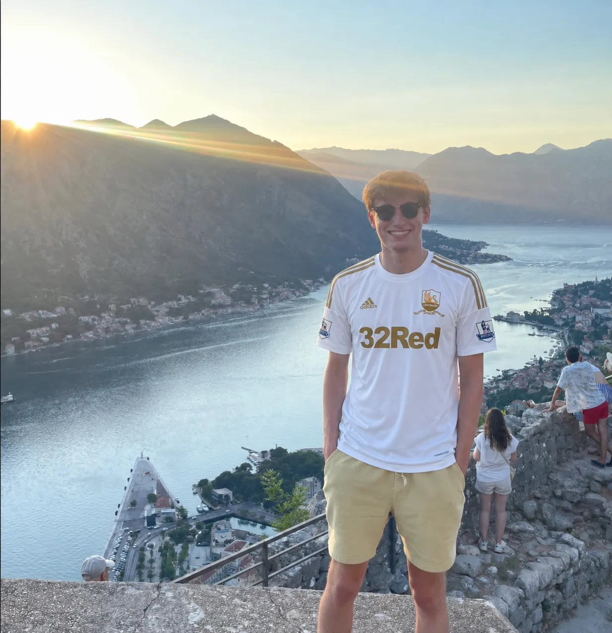 Reece Derrick standing above the Bay of Kotor at sunset, wearing a Swansea City kit