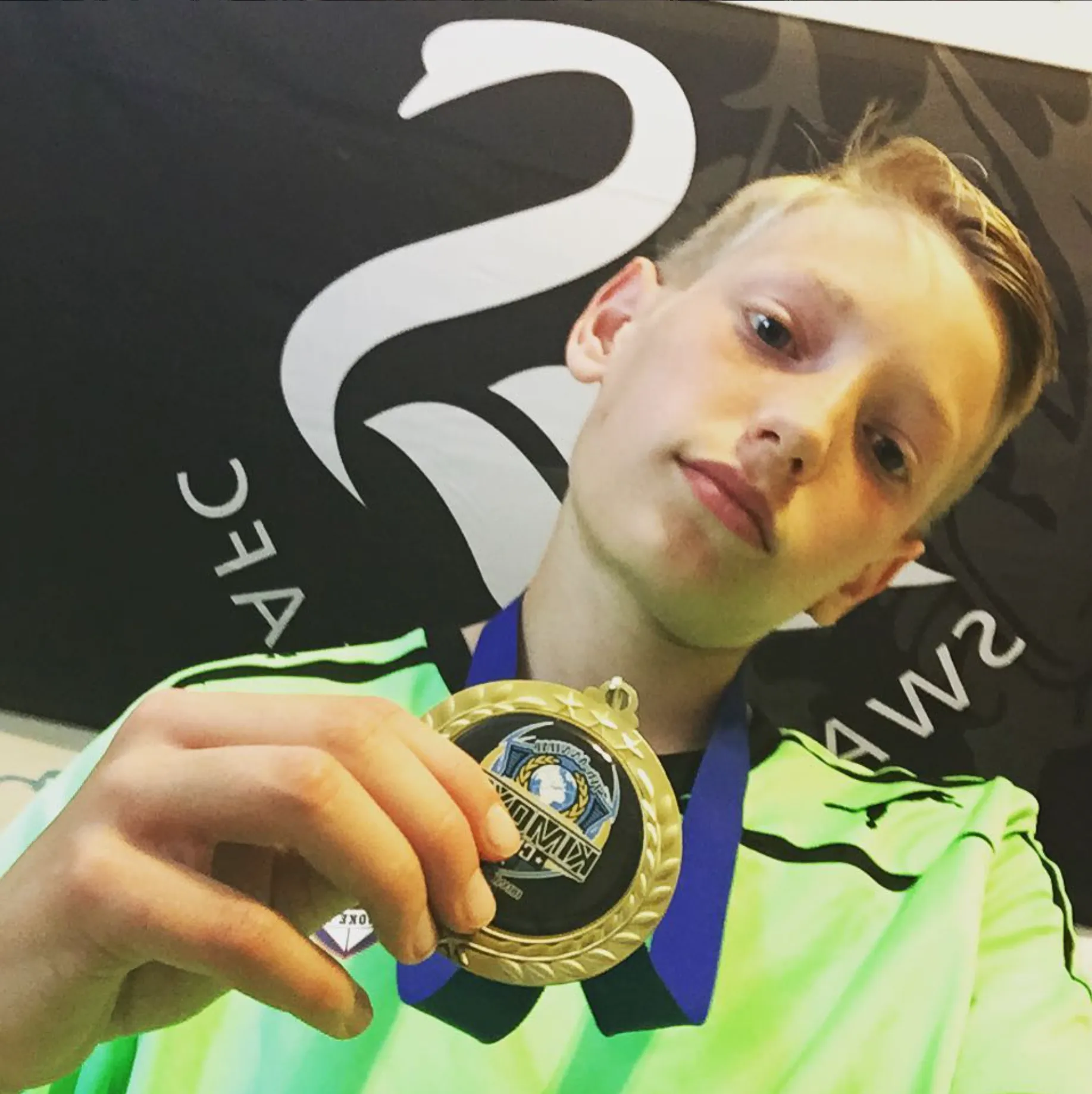 Reece holding a gold medal in front of a Swansea City swan banner